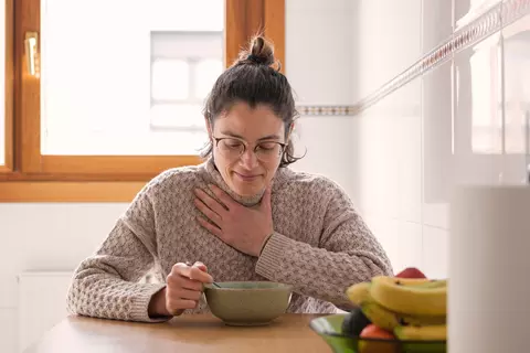 Frau mit Halsschmerzen isst eine Suppe